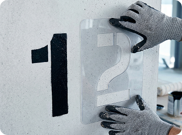 рабочий наносит цифры с помощью трафарета из пластика